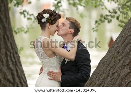 Just married couple kissing between tree trunks and pond