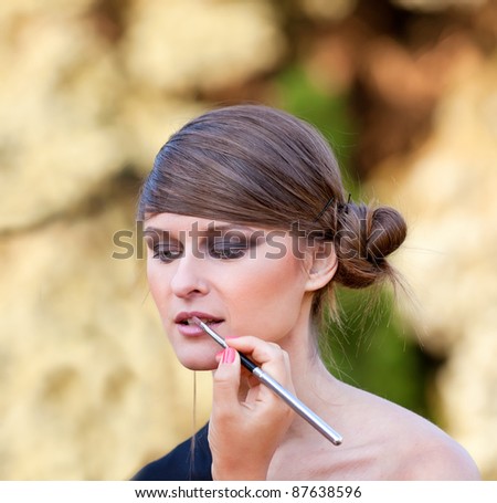 Makeup master applying lipstick with brush on caucasian girl lips