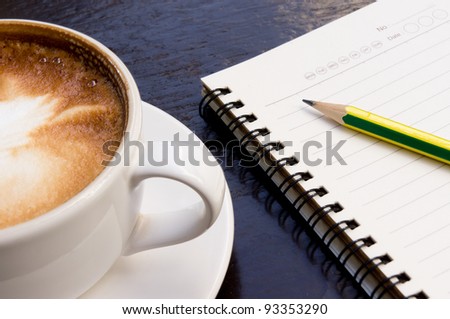 White cup of hot coffee latte and note book on dark wooden table