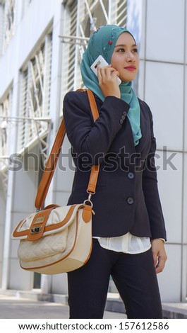 traveling business woman walking on train station platform with travel bag using mobile phone