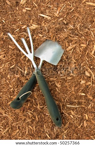 A picture of two garden tools crossed and sitting on fresh bark mulch