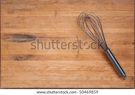 A worn butcher block cutting board sits as a background with a wire whisk to one side.