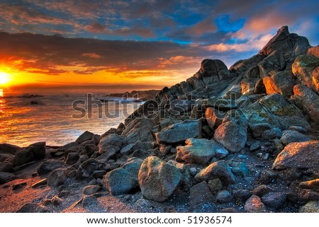 The sun is just rising over a rock filled California beach showing the golds and reds.