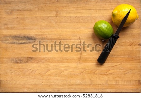 A lemon and a lime sit waiting to be cut with a knife on a worn butcher block cutting board