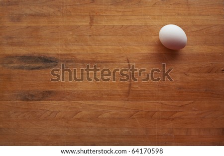 A single white egg sits on a butcher block counter with area suitable for text