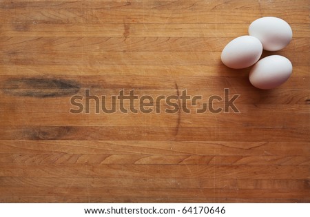 Three white eggs sit on a butcher block counter with area suitable for text