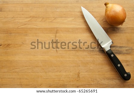 A view looking down on a large knife and onion on a worn butcher block cutting board.