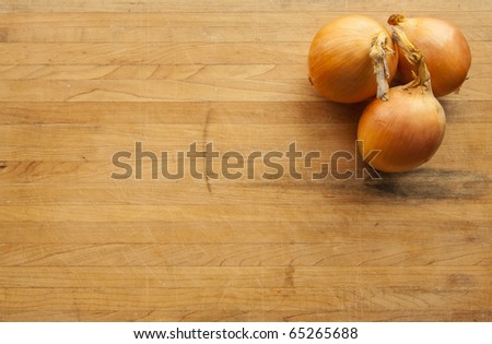 A view looking down on a group of three onions on a worn butcher block cutting board with room for text