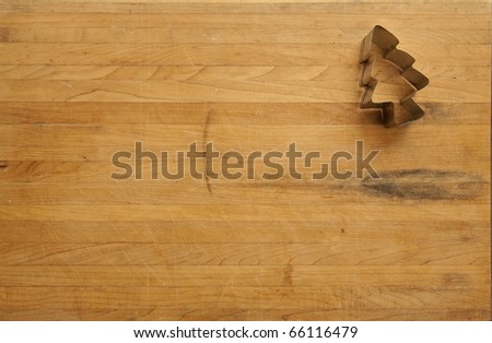 A view looking down on a single metal Christmas tree cookie cutter on a worn butcher block cutting board