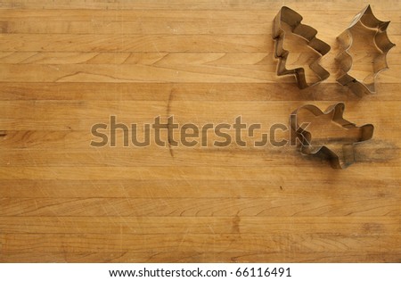 A view looking down on a group of three Christmas cookie cutters on a worn butcher block cutting board
