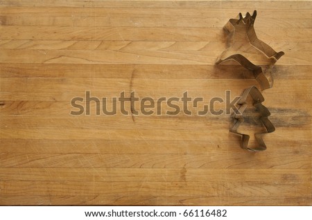 A view looking down on a metal reindeer and Christmas tree cookie cutter on a worn butcher block cutting board