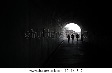 Silhouette of 4 persons walking through a dark tunnel towards the light at the end