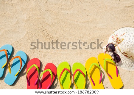 Row of colorful flip flops, sunglasses, floppy hat on beach