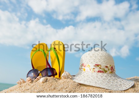 Yellow flip flop, sunglasses and floppy hat at the beach