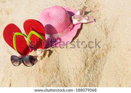 Red flip flop with sunglasses and pink floppy hat on beach