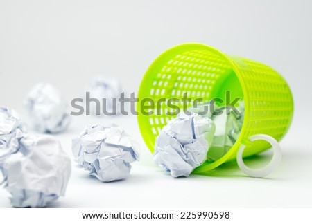 Green trash bin and crumpled paper balls on white background