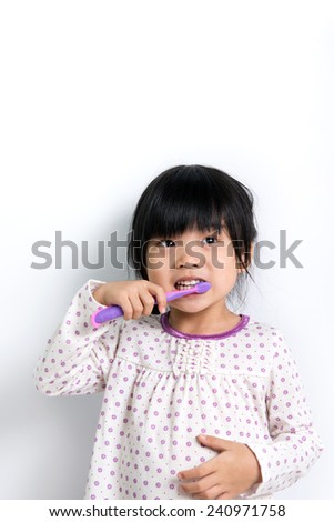 Little Asian girl in pyjamas brushing teeth