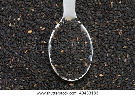 Black sesame seeds in a spoon on sesame pile