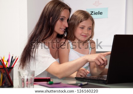 Attractive young mother teaching her beautiful smiling little daughter on a laptop computer pointing something out to her on the screen