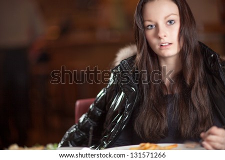 Candid portrait of an attractive serious sincere young woman sitting at a dining table looking at the camera, with copyspace