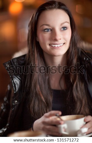 Beautiful attentive woman with a lovely smile looking up listening to someone off frame while enjoying a cup of cappuccino in a restaurant