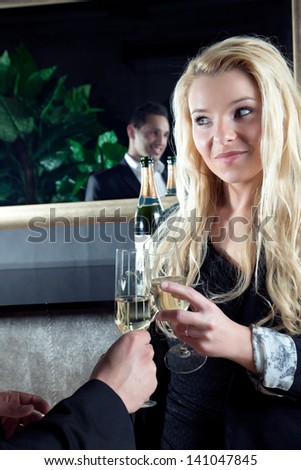 Beautiful young blond woman toasting her partner, a handsome man who is reflected in the mirror, with flutes of golden champagne as they celebrate a special moment