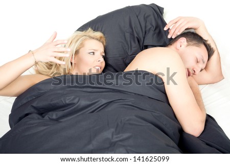 Angry frustrated woman in bed raising her fist as though to strike her sleeping husband following an argument or in an effort to quieten his snores