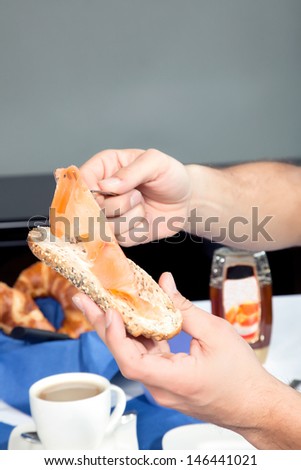 Hands of a man seated at a table selecting sliced cold ham for his buttered wholewheat roll