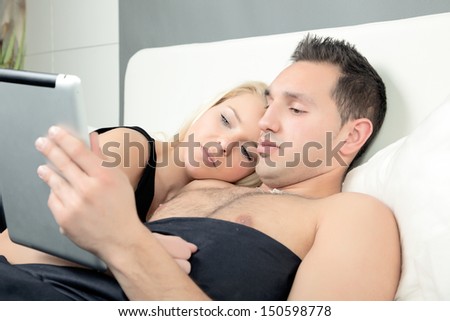 Couple snuggling in bed reading an e-book on a tablet-pc as they relax for the night