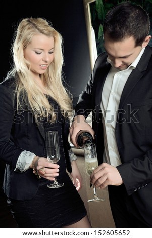 The Business Gentleman is filling the glass with sparkling wine while the young lady is holding the other glass.