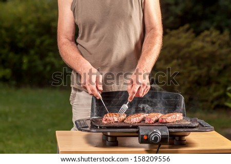 A man is grilling at a sunny day on a electric grill.