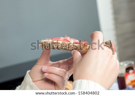 Closeup view of the hand of a young woman wearing a large ring eating a ham roll