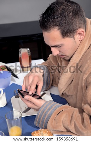 Closeup view of a man dressed in a dressing gown using his mobile at breakfast scrolling with his finger on the touchscreen