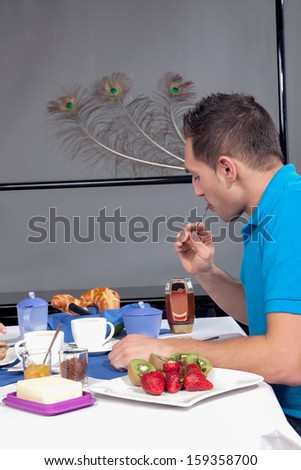Young man eating european style continental breakfast of croissants and strawberries