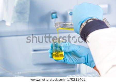 The analytical chemist is decanting a yellow dangerous liquid into an other test glass.