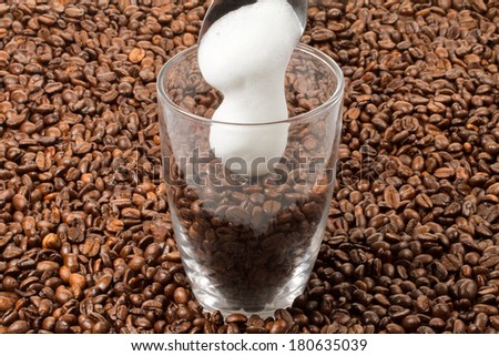 A milk froth is falling into a glass of beans decorated with a lot of java beans.