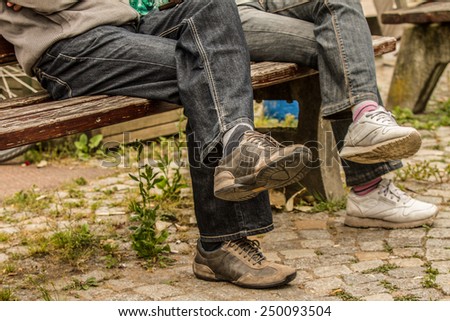 A couple is sitting outside on an park bench. Both crossed there legs