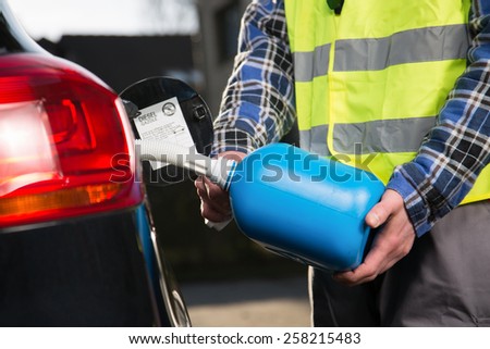 A man with a reflective vest is fueling a vehicle with a plastic canister.