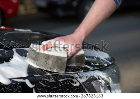 A man is washing his car with a sponge on the road.