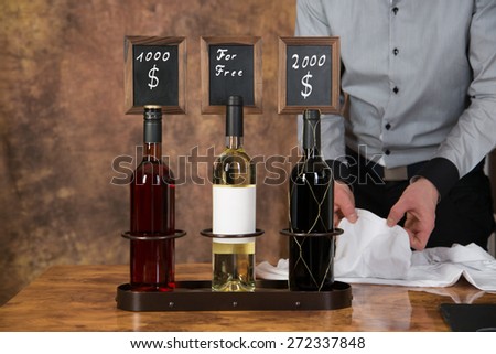 A waiter is decorating three wine bottles with a price board for selling