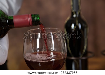 A Waiter is pouring red wine into a glass with a bottle of red wine in the background.