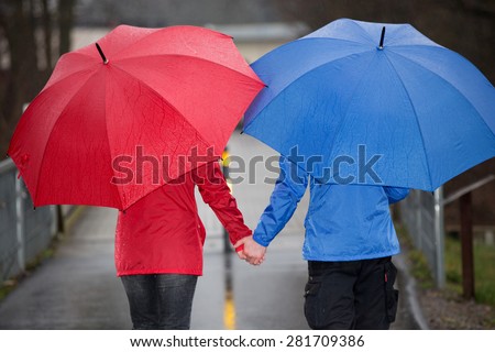A couple is walking hand in hand through the rain with umbrellas and rain cloth.