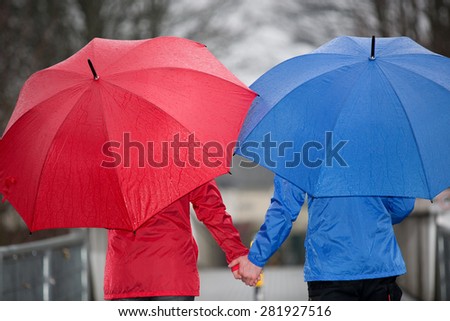 A close view from a walking couple hand in hand through the rain with umbrellas and rain cloth.