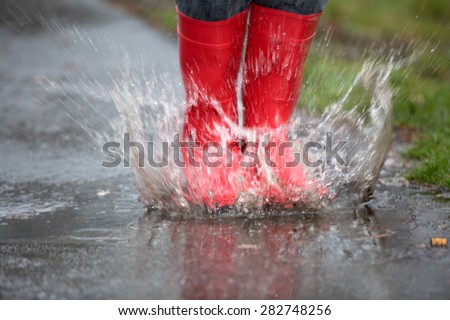 Rubber boots are jumping into a big puddle with splash.
