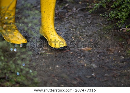 A pair of yellow boots in a muddy puddle during a rainy day.