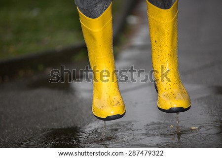 A pair of yellow boots are jumping into a puddle.