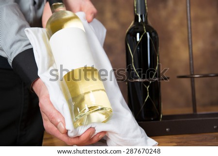 A waiter is presenting a bottle of white wine with a blank label.