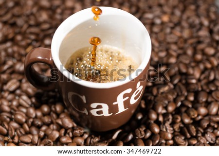 Some coffee drops are falling into a cup, decorated with coffee beans.
