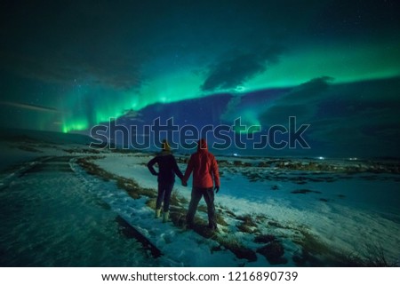 Couple watches the northern lights. Woman and man at winter night landscape . Iceland.