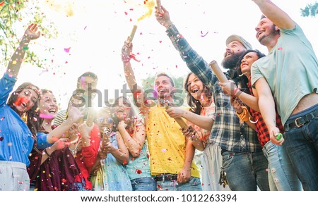 Happy friends having party,throwing confetti and using smoke bombs colors outdoor - Young students laughing and celebrating together - Youth concept - Main focus on three right guys faces
